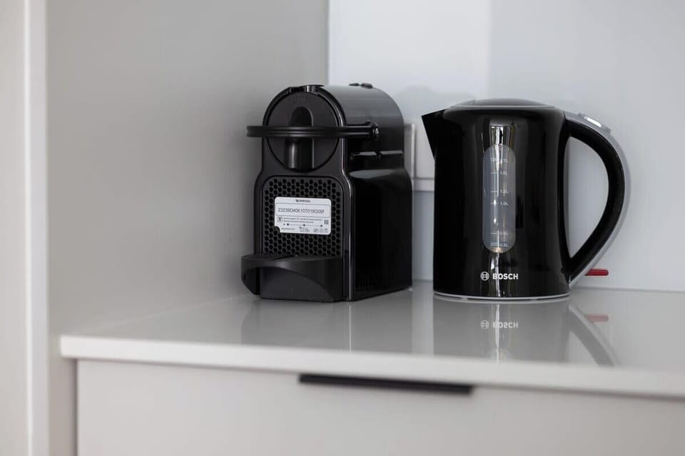 A close-up of a black coffee maker and kettle placed on a white shelf.