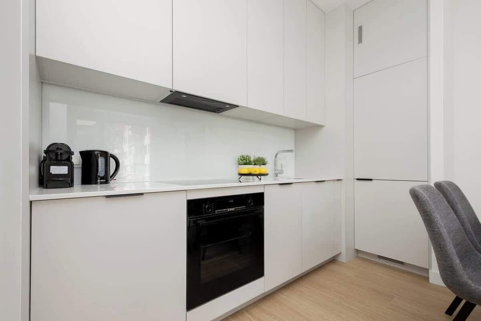 A minimalist kitchen with white cabinets, a built-in oven, and small appliances like a kettle and coffee maker.
