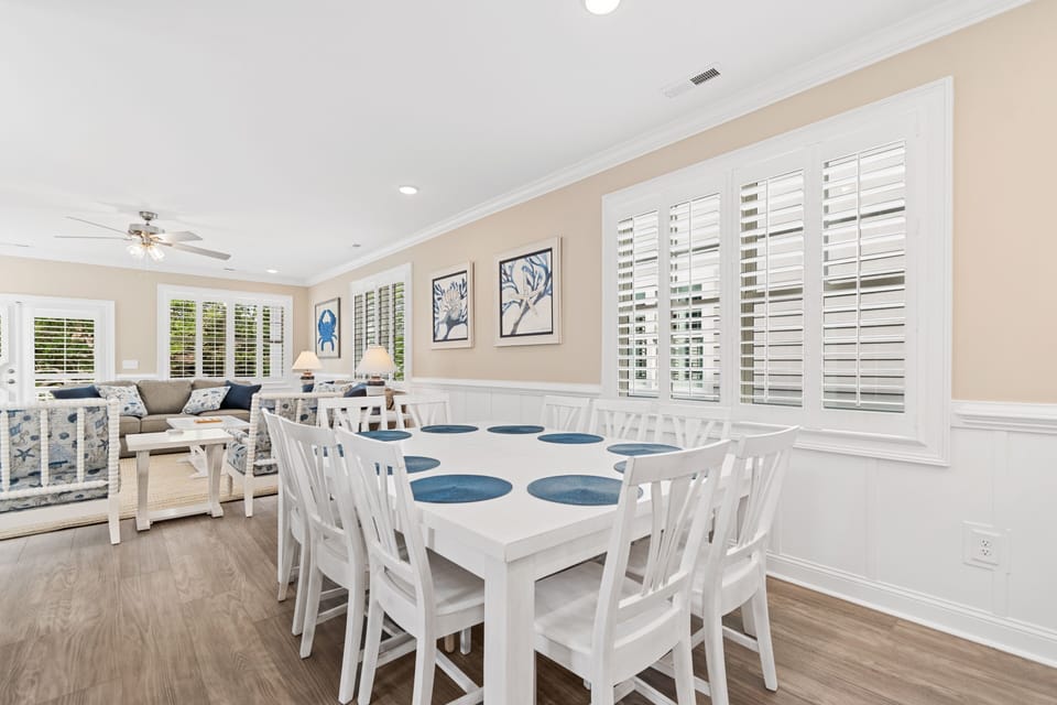 Your elegant dining space flows seamlessly into the living area, with white plantation shutters filtering natural light over the spacious table for eight.