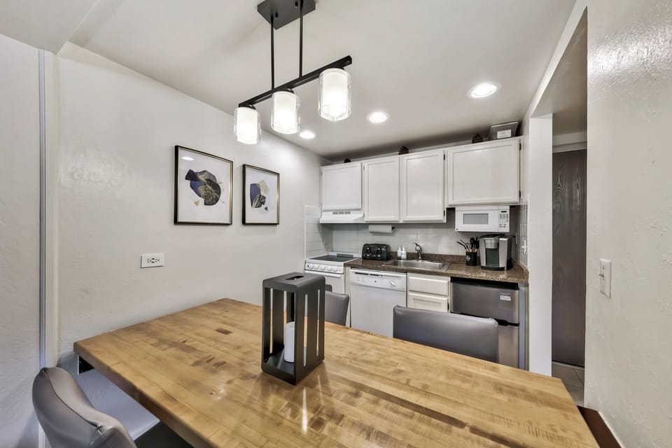 Your stylish dining area flows seamlessly into a fully-equipped kitchen, perfect for preparing meals and gathering around the beautiful wooden table.