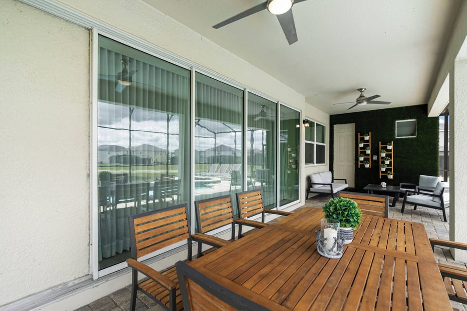 Step onto the spacious covered patio featuring a rustic wooden dining table, perfect for al fresco meals. With sleek ceiling fans and lush greenery, it's an ideal spot for relaxing or entertaining by the pool.