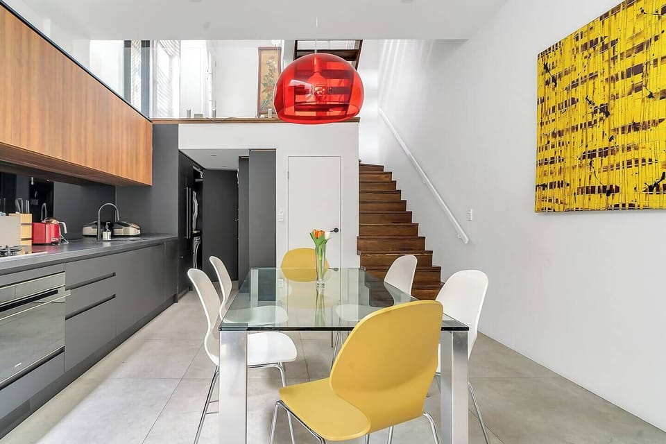  The dining area adjoins the open-plan kitchen and features a stylish glass table with white and yellow chairs seating six guests. 
