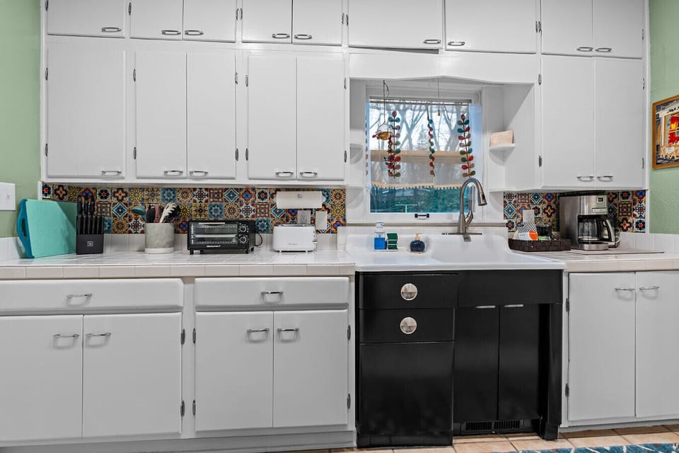 Modern Kitchen with Colorful Backsplash: Fully-equipped kitchen featuring vibrant tile backsplash and black appliances – Cairo St Bungalow Springfield, MO.