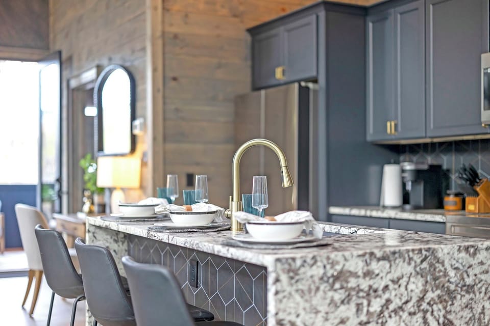 Modern kitchen with marble island, elegant place settings, and gold fixtures.