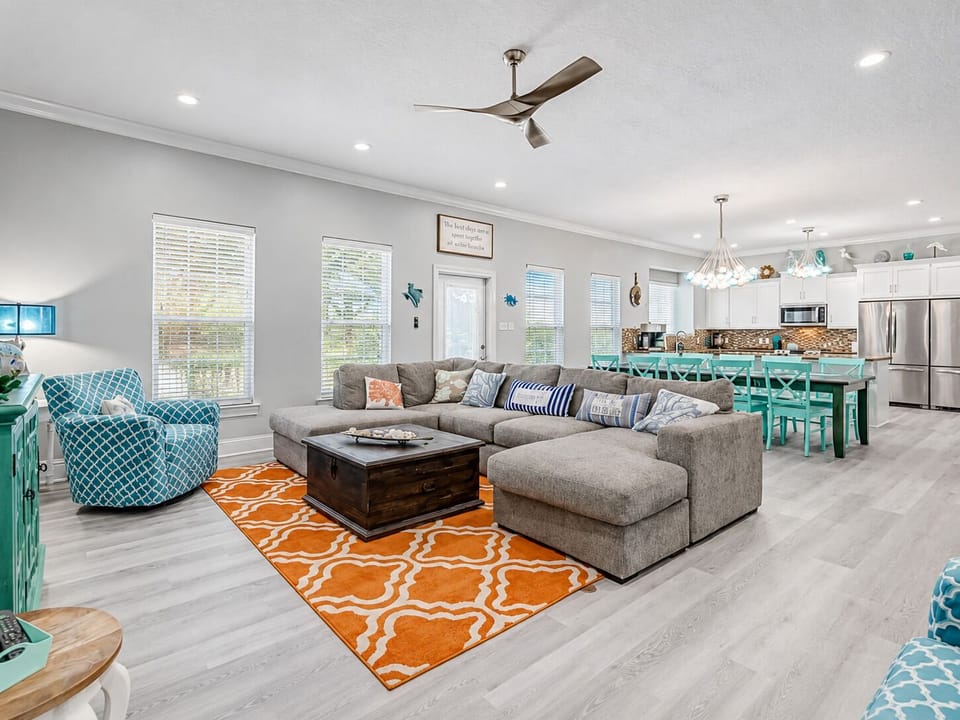 Spacious open floor plan connecting the living room, dining area and kitchen, with bright coastal décor and plenty of seating for large vacation groups.