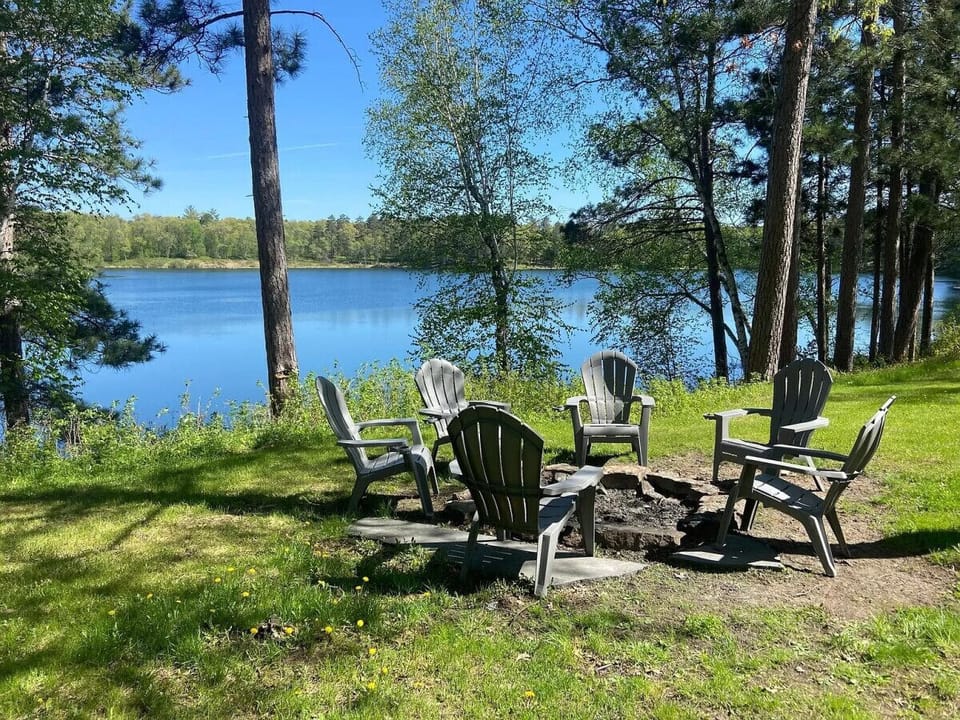 Lakeside bonfire area featuring Adirondack chairs and a scenic view.
