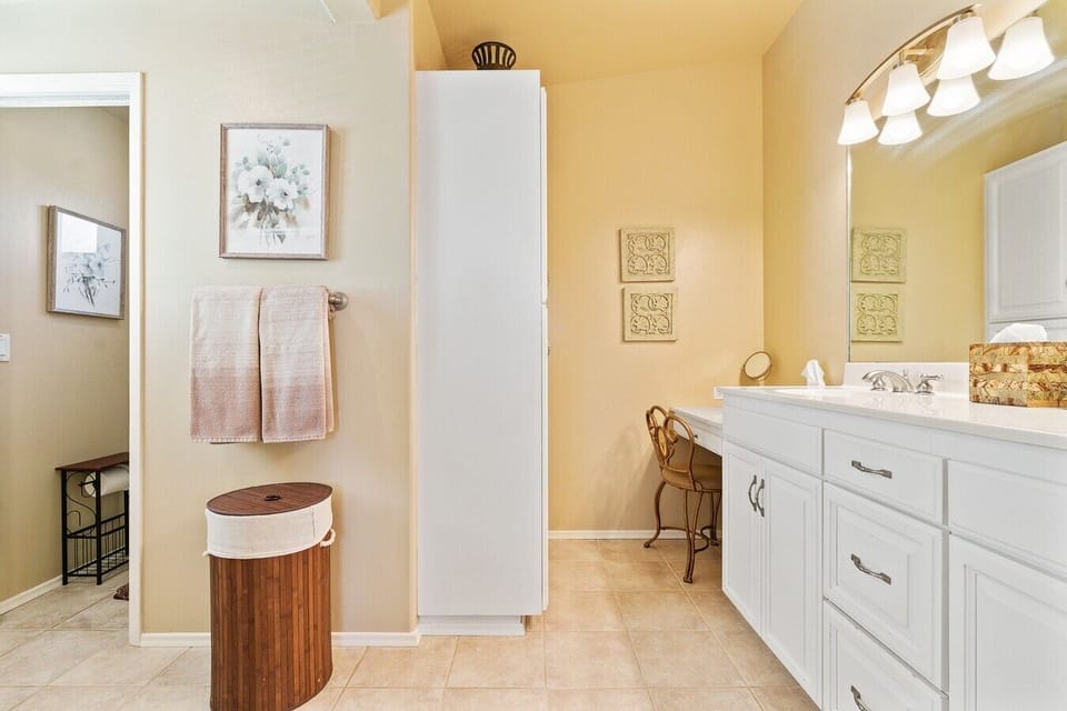 En-suite bathroom with a private vanity desk, linen tower, and soft, sunlit finishes.