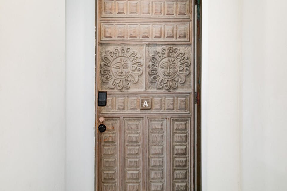 A beautifully crafted wooden door featuring intricate sun carvings and unique geometric patterns, marking the entrance to a charming and distinctive living space. The door`s artistic design adds a touch of character and warmth to the entryway.