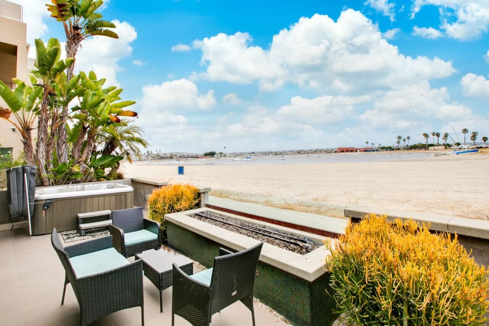 A luxurious beachfront patio featuring a comfortable seating area with wicker furniture, a private hot tub, and seamless access to the indoor living space. The patio is designed for relaxation and entertainment, offering stunning views of the beach and lu