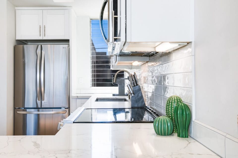 A close-up view of a modern kitchen featuring a sleek marble countertop, stainless steel appliances, and a glossy subway tile backsplash. The stylish and functional space is accented with decorative elements, such as small ceramic cactus plants, adding a 