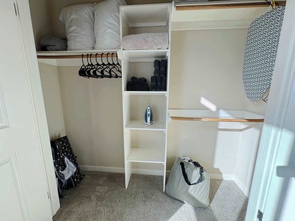 Spacious closet stocked with additional sheets, pillows, blankets, iron, ironing board, and a crib.