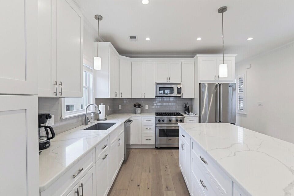 Whip up a meal in the fully equipped kitchen, featuring sleek white shaker cabinets, elegant quartz countertops, and modern stainless steel appliances. A spacious central island provides additional prep space and casual seating.