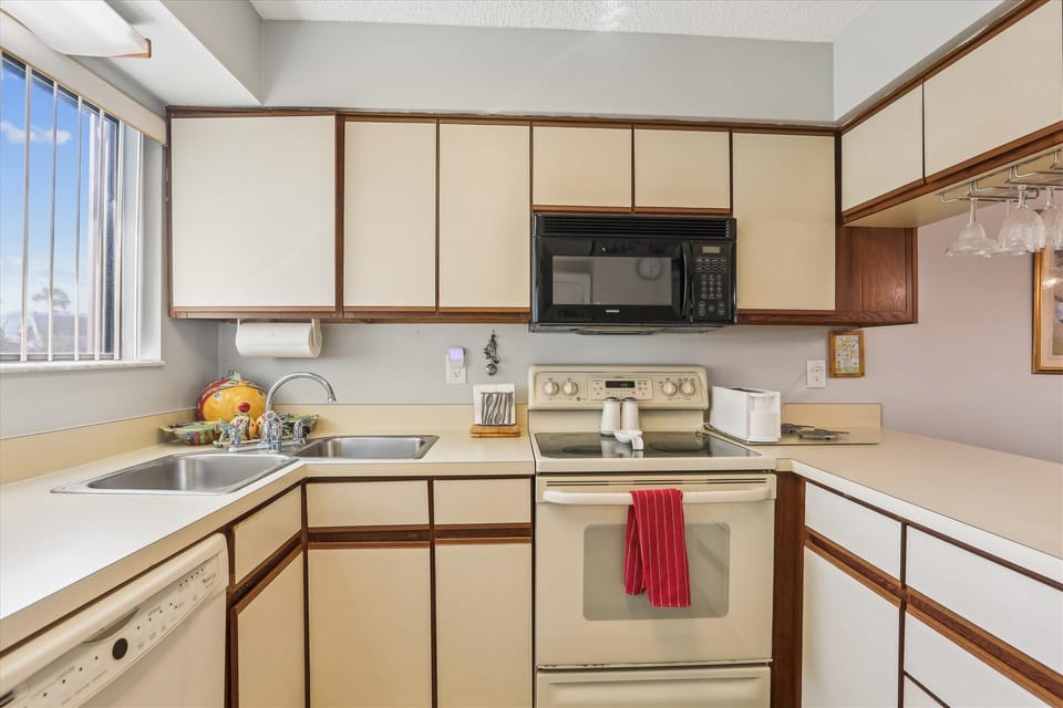- Full kitchen with stove, oven, and microwave set among neutral cabinetry
- Spacious counters and sink area offer convenience for meal prep and cleanup
- Bright window light enhances the space making it inviting for cooking
