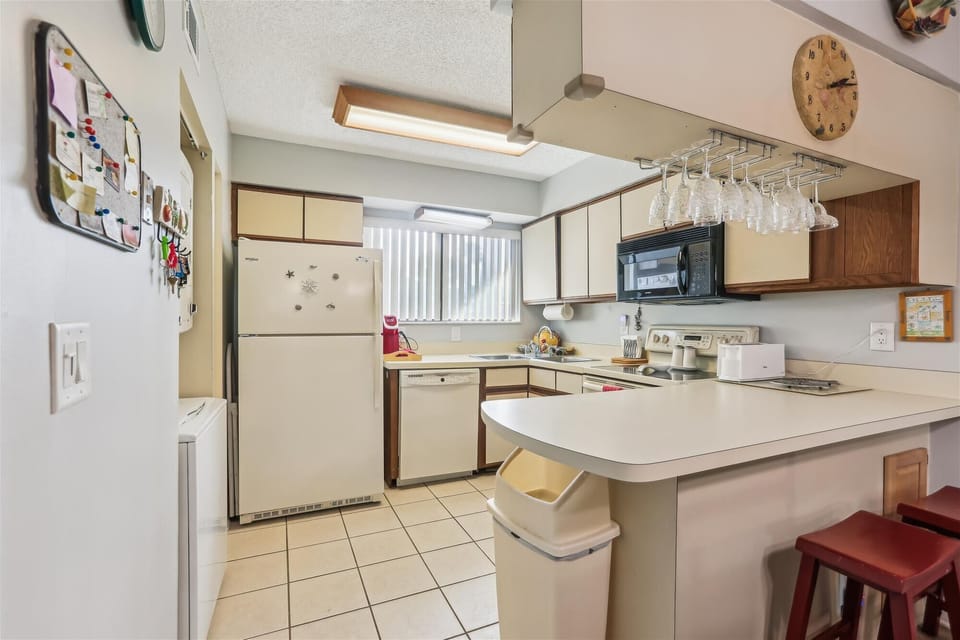 - Full kitchen with white appliances, microwave, and spacious countertop area
- Bar seating with stools and hanging glasses makes casual dining effortless
- Bright window fills the space with light for easy cooking and gathering
