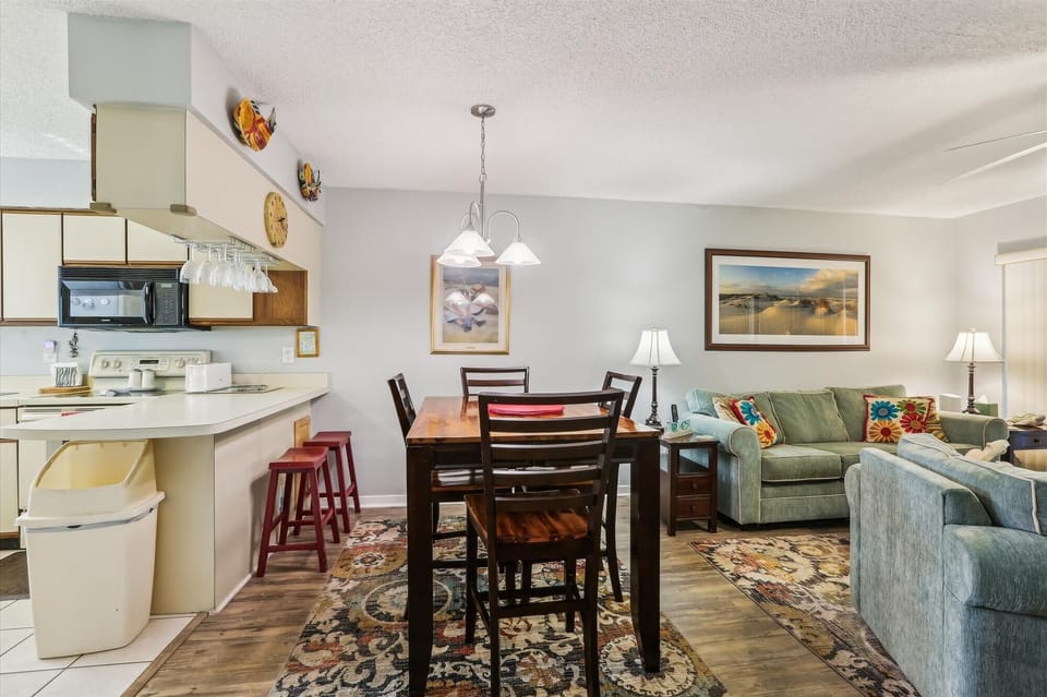 - Open concept dining and living space with seating for meals and gatherings
- Sofa, armchairs, and decor create a relaxed environment for family time
- Overhead lights brighten the space for both day and night enjoyment