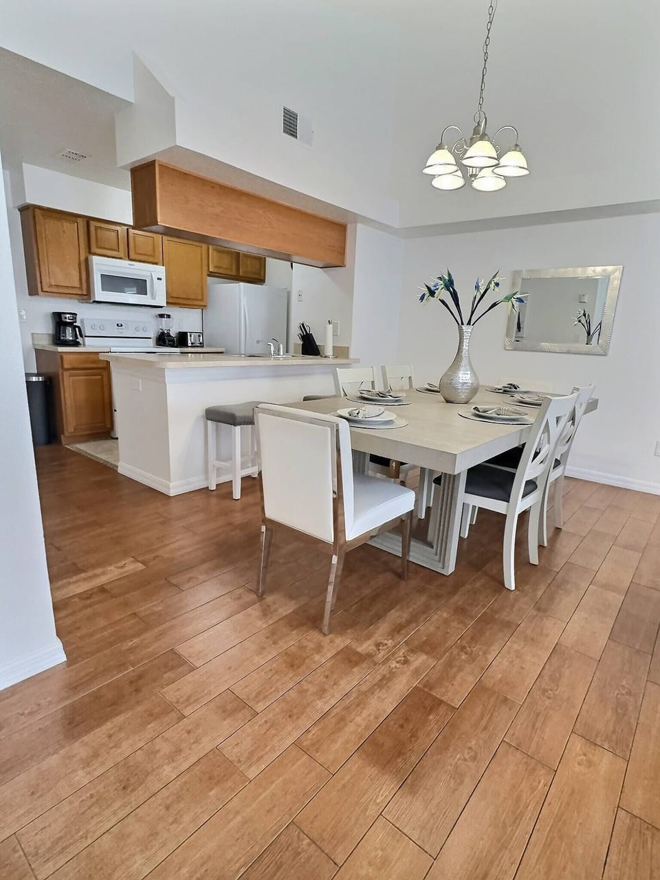 Bright and airy, this dining area features a chic table set for memorable meals, complemented by stylish white chairs and warm wood flooring. The open layout seamlessly connects to the kitchen, inviting effortless gatherings.