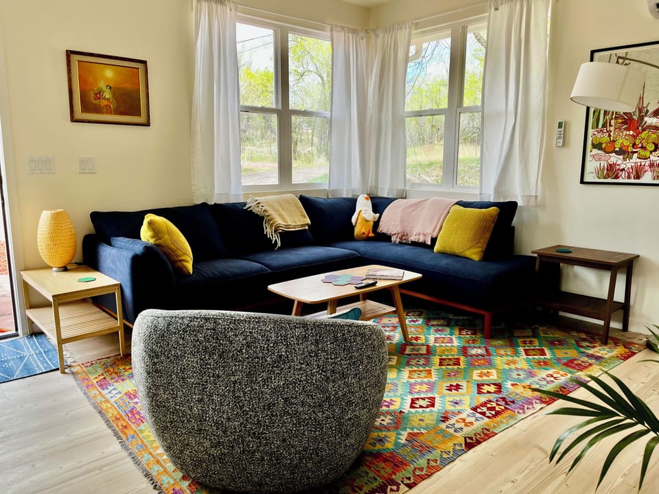 Light, comfy, living room with 75 inch tv and windows facing nature.