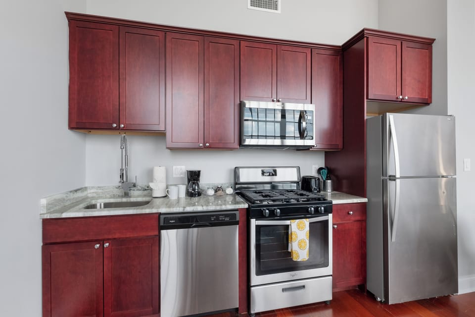 Fully equipped modern kitchen with distinctive red cabinetry, stainless steel appliances, and granite counters—perfect for meals or entertaining.