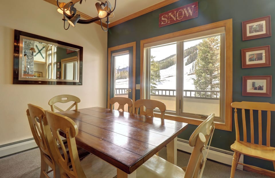 A cozy dining room with a wooden table, large windows and door allowing ample natural light in.