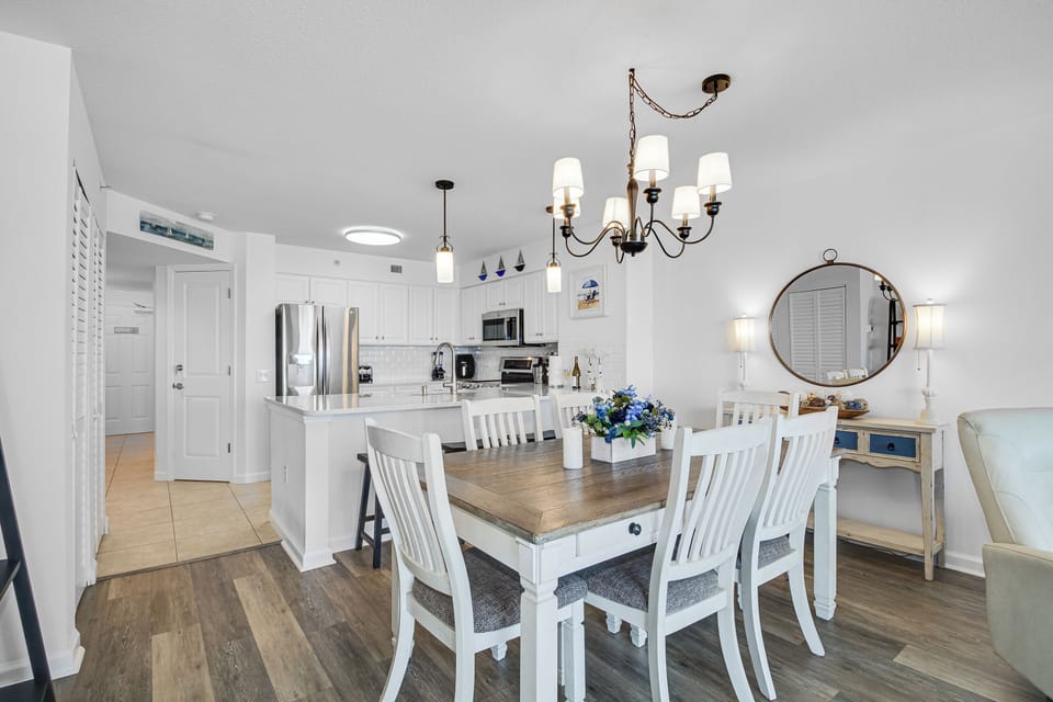 Gather around your elegant dining table beneath the warm chandelier, while the fully equipped kitchen awaits your culinary adventures in this bright, coastal-inspired space.