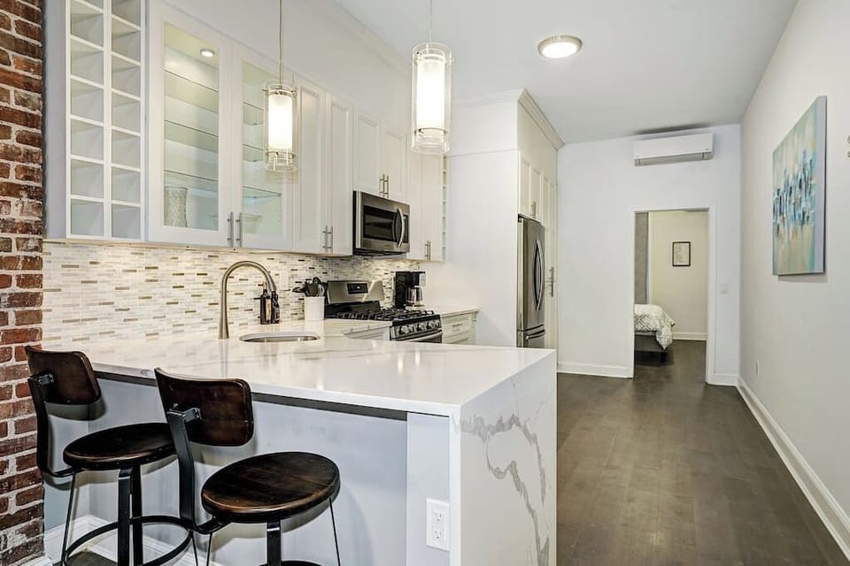 The kitchen features stainless steel appliances, white shaker-style cabinetry, and Calacatta Borghini quartz countertops with a waterfall edge