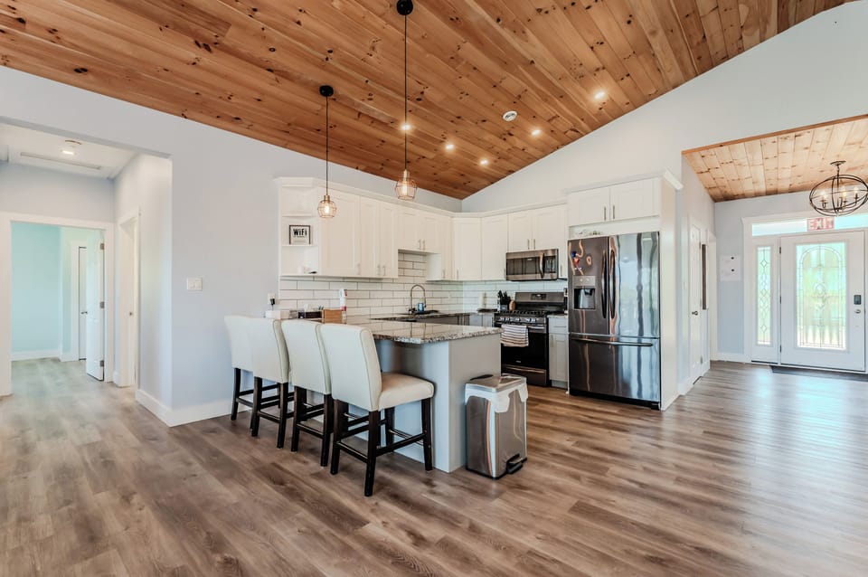 The living room features a cozy fireplace and built-in shelves filled with books and games. The warm wooden ceiling and expansive layout make this area a perfect spot for relaxing and enjoying quality time with loved ones.