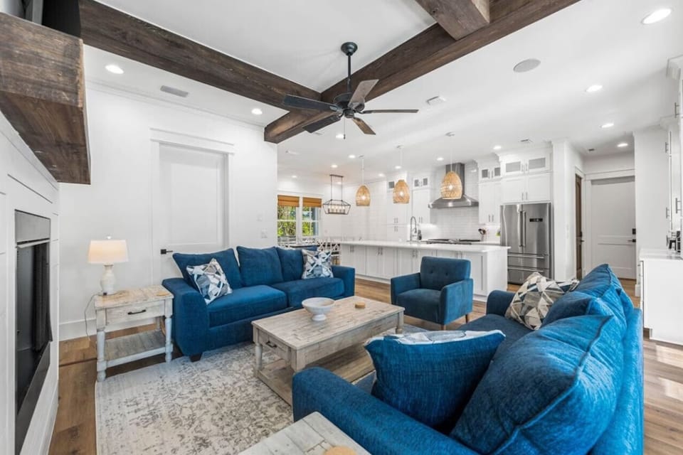 Relax in your stylish living space with plush blue seating and rustic wooden beams overhead, flowing seamlessly into a fully-equipped modern kitchen.