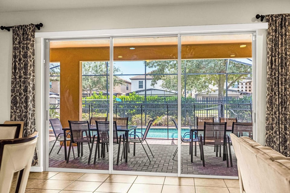 Private poolside patio with ample outdoor seating, a screened enclosure, and a turquoise swimming pool surrounded by lush greenery.