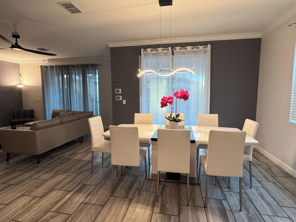 Private dining room with seating for a group, a modern looping pendant light, and a vibrant orchid centerpiece beside the comfortable living area.