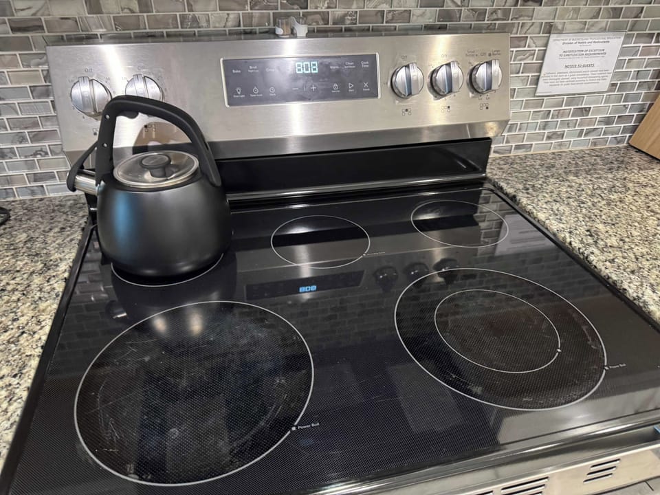 Well-equipped kitchen with a four-burner electric range, black kettle, granite counters, and a modern mosaic tile backsplash.