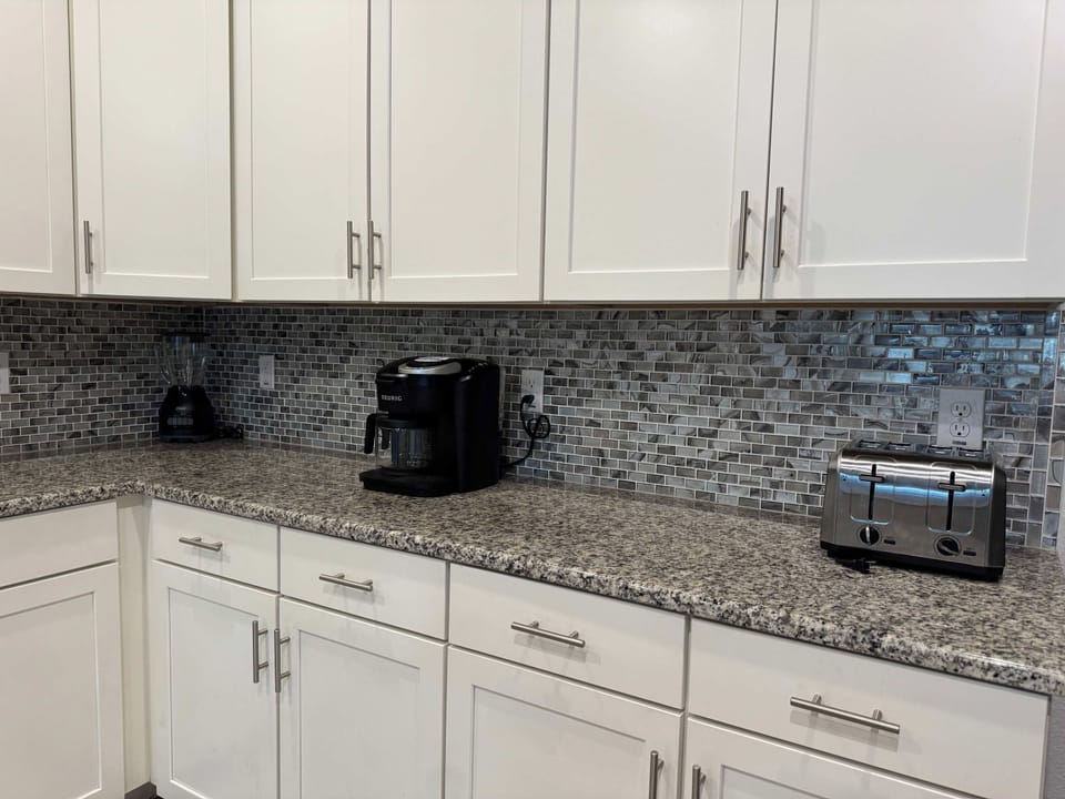 Well-equipped kitchen with white cabinetry, granite counters, a coffee maker, blender, and stainless-steel toaster.