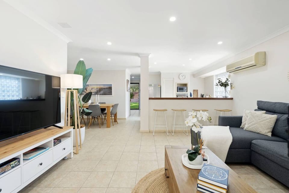 This open-plan space seamlessly combines a comfortable living area with a large smart TV, a stylish dining zone for shared meals, and a convenient kitchenette with a breakfast bar. 