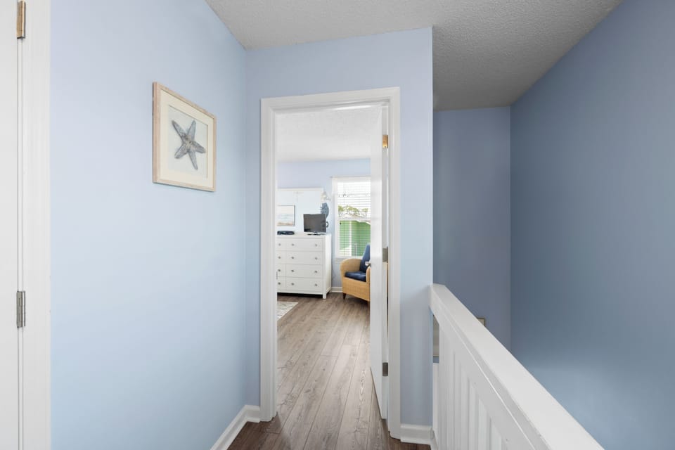 Step through this calming blue hallway into your coastal retreat, where starfish artwork and warm wood floors welcome you home.