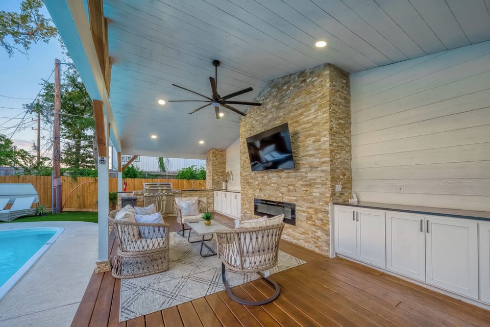 Luxury patio with TV, fireplace, outdoor kitchen, and poolside seating.