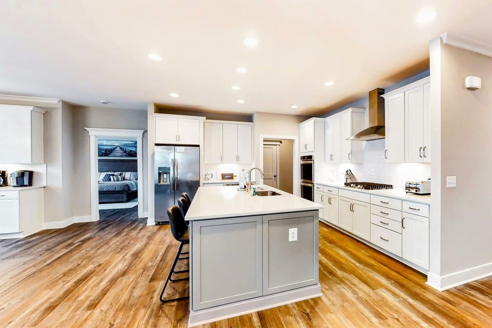 A modern kitchen features white cabinetry, stainless steel appliances, a central island with bar stools, and warm wooden flooring