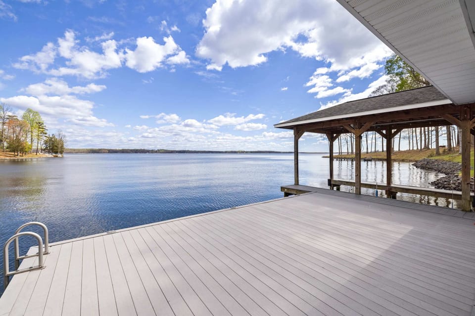 A spacious wooden dock extends over calm lake waters under a vast sky with fluffy clouds, offering a peaceful setting