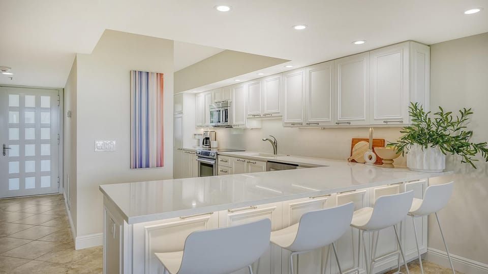 Recessed lighting illuminates the white kitchen with stainless steel oven, microwave, and a plant centerpiece on the counter.