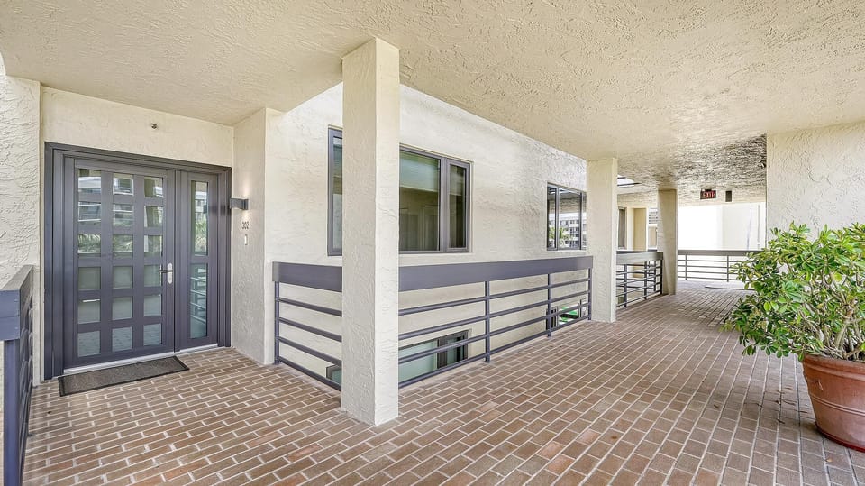 Brick-patterned tile flooring extends through the covered walkway leading to the condo’s gray double entry doors.