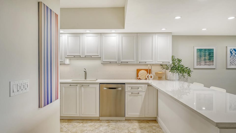 White cabinetry lines the kitchen with a stainless dishwasher, marble countertops, and recessed ceiling lights.