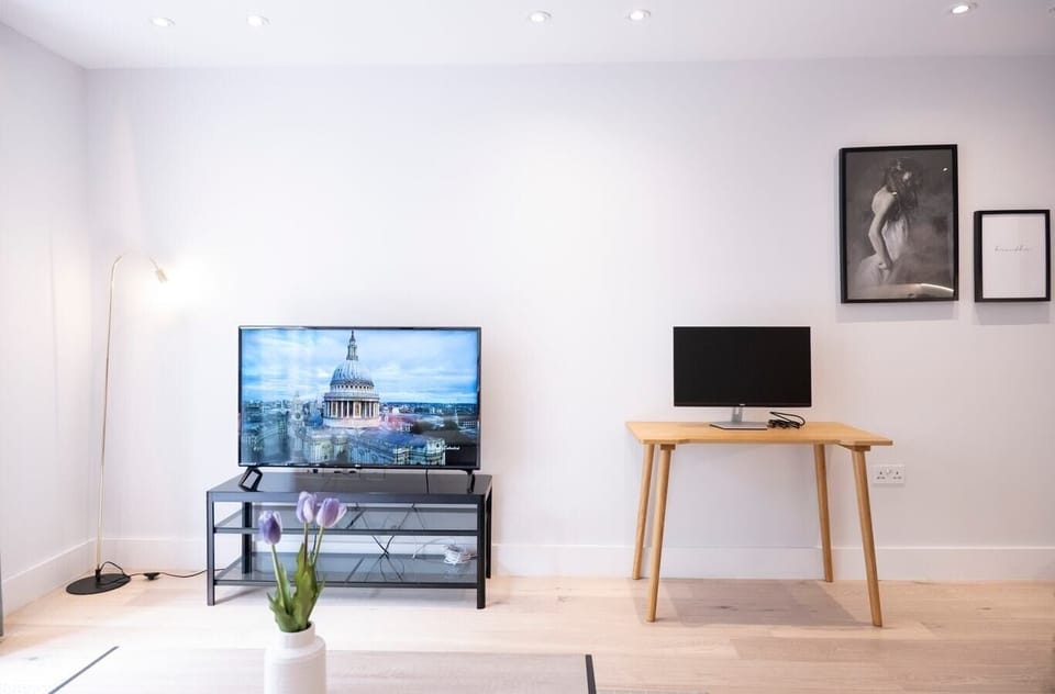 Open-plan living room with a fully equipped kitchen, sofa bed suitable for the 5th and 6th guests,  a dedicated desk with a 27-inch monitor, and a smart TV.