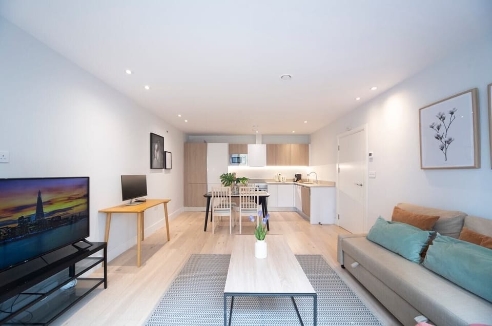 Open-plan living room with a fully equipped kitchen, sofa bed suitable for the 5th and 6th guests,  a dedicated desk with a 27-inch monitor, and a smart TV.