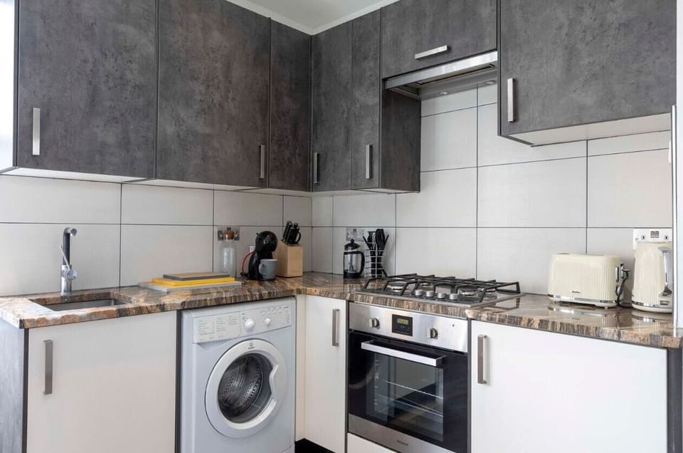 Fully equipped kitchen with washing machine, stovetop, oven, fridge, kettle, and toaster.
