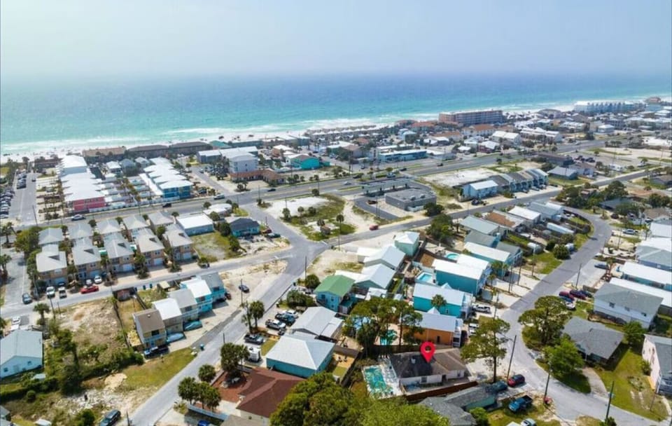 Aerial view of a charming coastal community featuring colorful homes nestled between pristine white sand beaches and peaceful residential streets.