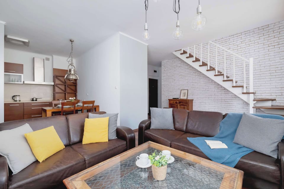 Open-Concept Lounge and Dining Area
Bright and spacious area combining dining and living zones, featuring exposed brick and a staircase to the upper level.