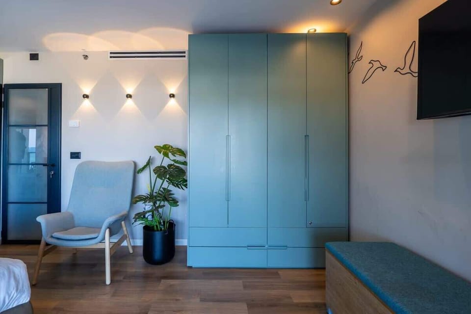 The bedroom features a comfortable lounge chair, a large wardrobe for practical storage (including shelves, a hanging space, and drawers), and a smart TV.