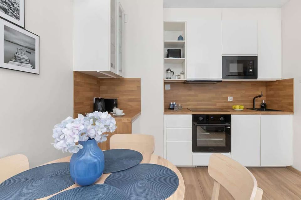 A modern kitchen with white cabinetry, wooden countertops, and a small round dining table with a vase.

