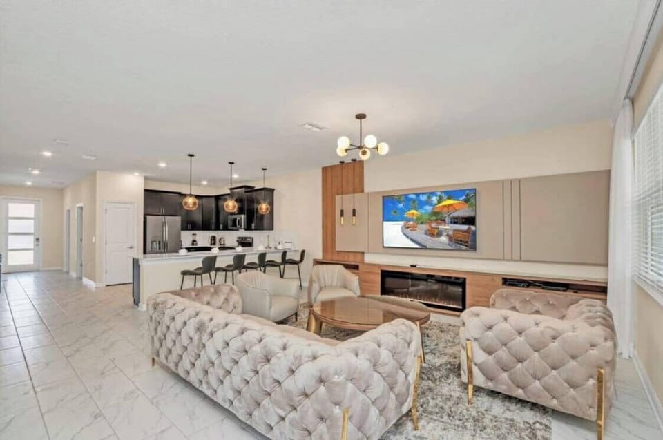 Experience the inviting charm of this airy living room featuring plush tufted sofas and warm wood accents, seamlessly flowing into a stylish kitchen illuminated by elegant pendant lighting, creating the perfect gathering space.