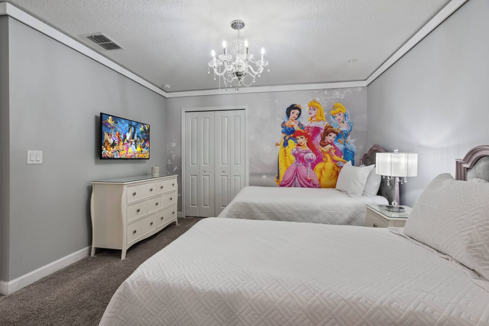 Welcome to a delightful bedroom with two cozy beds dressed in plush white bedding for restful nights. A charming chandelier adds sophistication, while a whimsical princess mural infuses fun and color into the space.