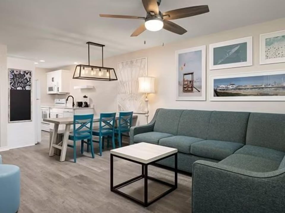 Teal sectional sofa and dining table with blue chairs in the open living area — coastal wall art throughout