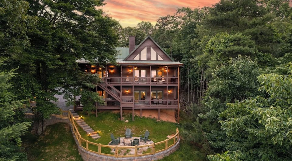 Wooded multi-story cabin with large windows, wooden siding, and wraparound deck.